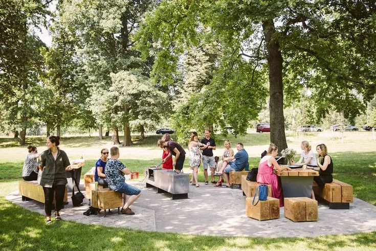 Birthday Party Ideas for Kids 6 Outdoor birthday party gathering in a green park with families and friends enjoying food around wooden picnic tables under large trees.